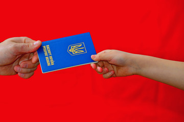 A man passes the passport of ukraine on a red background, hands accepting a document.