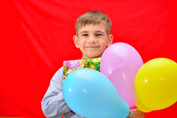 Fototapeta na wymiar A boy with a gift and balloons on a red background in the studio