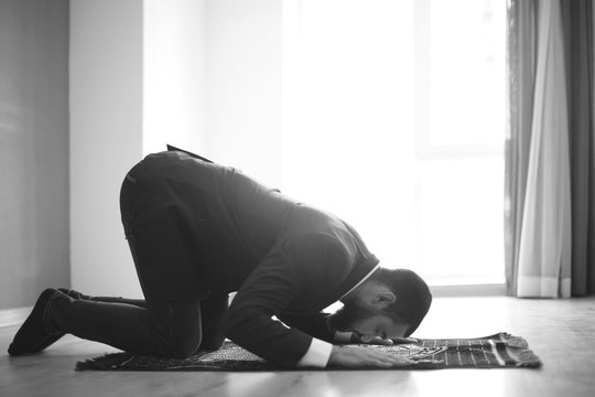 Young Muslim man praying indoors, toned in black and white