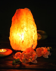 Himalayan salt lamp, candle and flowers on table against dark background