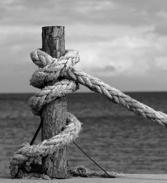Fototapeta Black and white rope on seafront, sea and cloudy sky