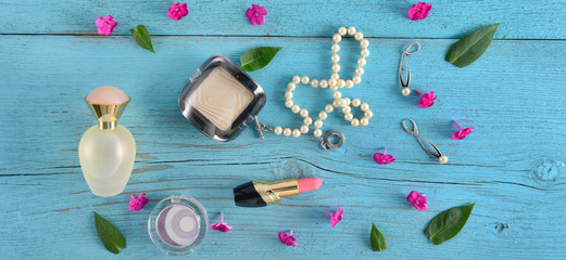 Cosmetics, perfumes and jewelry made of pearls on an old wooden background of blue color. Wide photo.