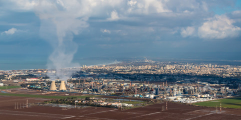 large Industrial chimneys at Refineries in Israel Haifa against green fields