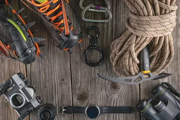 Gardinen Top view of rock climbing equipment on wooden background. Chalk bag, rope, climbing shoes, belay/rappel device, carabiner and ascender. Active lifestyle concept. © martingaal