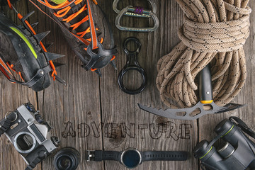 Top view of rock climbing equipment on wooden background. Chalk bag, rope, climbing shoes, belay/rappel device, carabiner and ascender. Active lifestyle concept.
