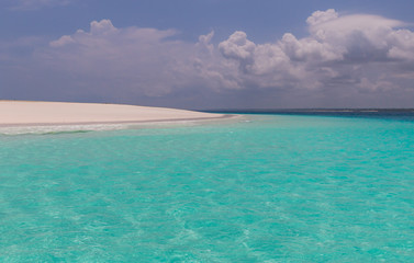 Naklejka premium Turquoise water blue sky on a tropical island. The sand is white and the water is calm and there are clouds in the sky. The water is crystal clear. There are green trees on the island .Zanzibar