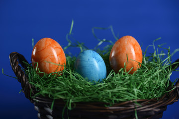 Painted Easter eggs of orange and light blue in green grass in a wicker basket.