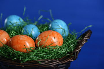Painted Easter eggs of orange and light blue in green grass in a wicker basket.