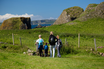Hiking family, mother and three children walks on green, grass covered field, North Ireland