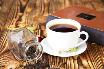 a white cup of tea on a wooden table, next to a book