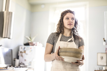 young woman prepares the table by carrying a stack of dishes in a bright kitchen