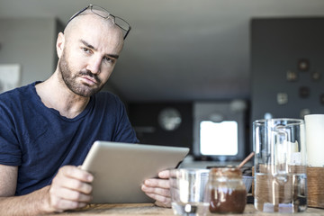 Portrait of a stylish man in his private home while is checking a to do list, working on his tablet and taking his break fast. Modern house and a business man in a private situation.