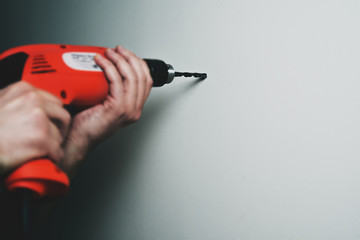 Drilling with a drill in the wall. Man holding a red drill in his hand, the concept of renovation, homemade needlework. Suspending shelves, arranging frames with photos, renovation in the apartment.