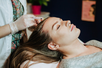 Naklejka premium Woman in cosmetology cabinet. Cosmetologist is doing injection. woman receives an injection in the head. The concept of mesotherapy. 