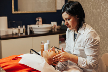 Obraz na płótnie Canvas Cosmetologist is going face mask / peeling for young woman. Woman is having cosmetology procedure 