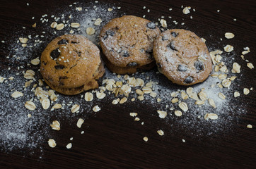 Cookies with chocolate on dark background with sugar powder, oat flakes and seasame
