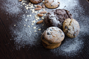 Cookies with chocolate on dark background with sugar powder, oat flakes, seasame and almond. Copyplace, place for text