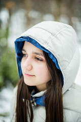 portrait of an 11-year-old girl outside under a snowfall, dressed in a down jacket, a windbreaker