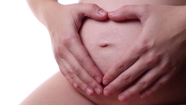 A pregnant woman makes a heart shape with her fingers on her stomach