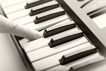 The finger presses the keys of the musical synthesizer