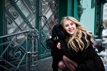 Fototapeta na wymiar Elegance blonde girl in fur coat hugs small black dog.