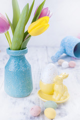 Spring tulips are pink and yellow. Different colors of eggs and pottery rabbit. Decor for Easter
