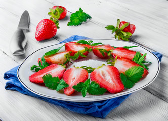 Slice of strawberry with leaf of mint and shugar on white plate