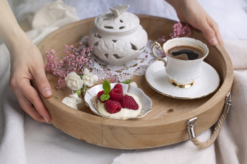 Morning coffee and flowers. Romantic breakfast in bed. A wooden tray in the hands. Home cosiness. Light background