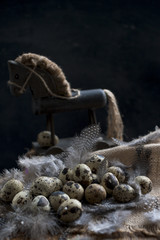 a lot of quail eggs and feathers, a wooden toy horse. Spring decor and Easter. Dark background and space for text. Country style