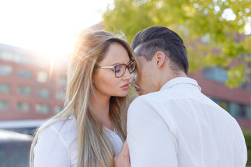 Young blonde woman whispers to man declaration of love outdoors