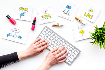 Female blogger concept. Work desk with keyboard, cosmetics and social media icons on white desk top view. Hand is typing