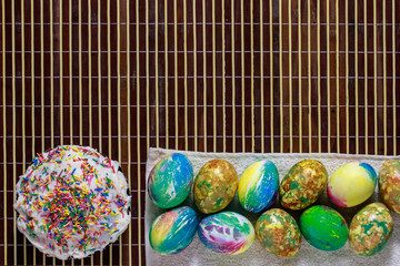 Kulich and a lot of colorful Easter eggs lying on a bamboo napkin