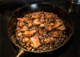 Beef Cooking and Sizzling in Cast Iron Frying Pan on Stove