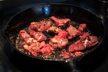 Beef Cooking and Sizzling in Cast Iron Frying Pan on Stove