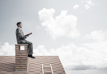 Student guy in suit on brick house roof reading book