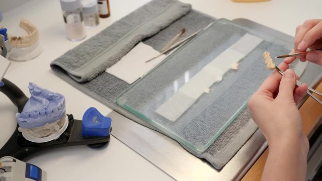 Dental prosthesis laboratory, specialist applies paint on artificial teeth close-up in workplace with tools