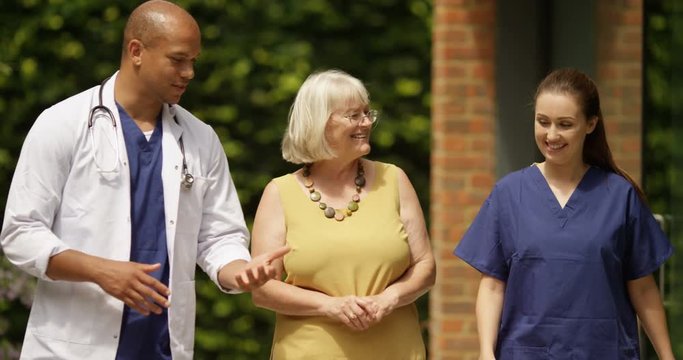 4K Medical staff walking with mature lady outside clinic, having a happy conversation. Slow motion