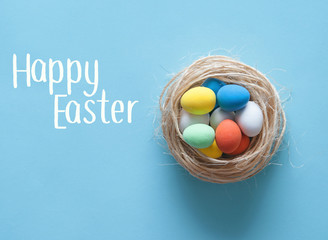 Mini colorful eggs in a nest on blue paper background. Happy Easter.
