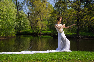 Fototapeta na wymiar Oriental woman in long white dress with train walking along the pond in the Park