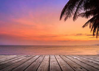 Naklejka premium Pusty drewniany taras nad tropikalną plażę z palmą kokosową o zachodzie słońca lub wschodzie słońca