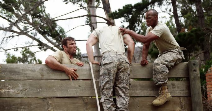 Male soldiers assisting their team mate to climb a wooden wall 