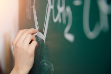 Chalk board. Close-up of human hand writes formulas on physics and chemistry in school and university.