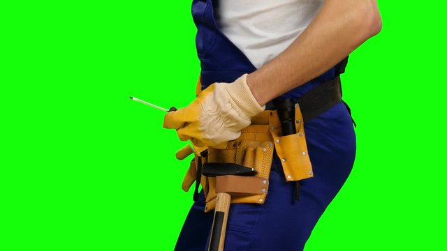 Worker takes out a screwdriver from his construction belt. Green screen. Side view. Close up