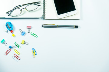 Top view of laptop, blank notebook, paper clips  and smart phone with white background and copy space.