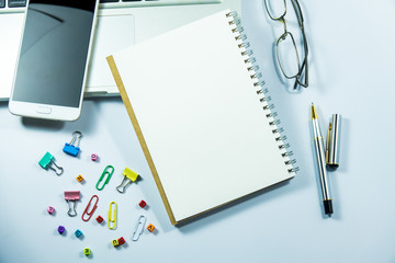 Top view of laptop, blank notebook, paper clips  and smart phone with white background and copy space.