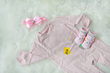 Collection items of bodysuits for newborn babies with socks on white fur background.
