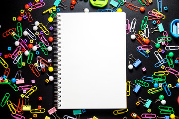 Top view of office table or desk with blank notebook and colorful equipment on black background with copy space for text.