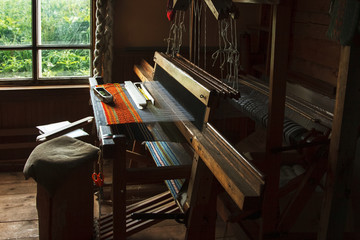 Handloom.
An antique vintage wooden machine in the interior of the workshop by the window.
