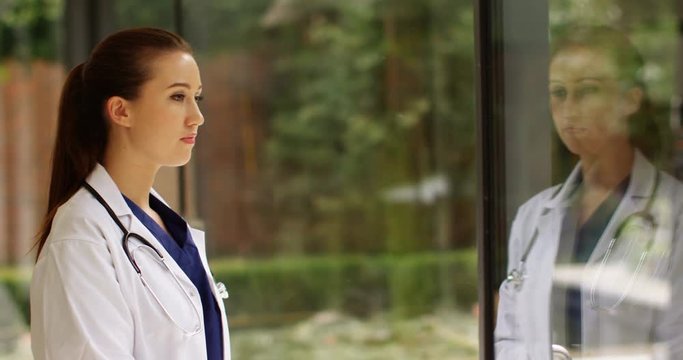 4K Beautiful doctor staring out of window, her image reflected on the glass. Slow motion