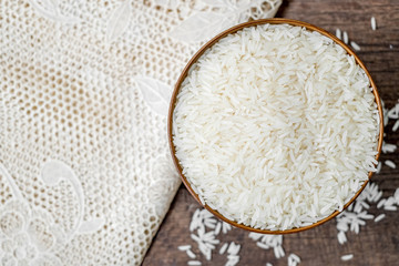 Rice in wooden bowl with white tablecloth on old wood texture background, Copy space